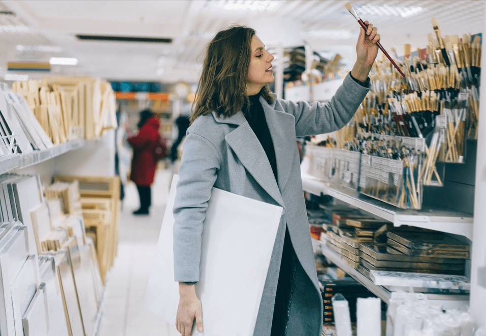 Mujer eligiendo un pincel en la sección de bellas artes de una tienda